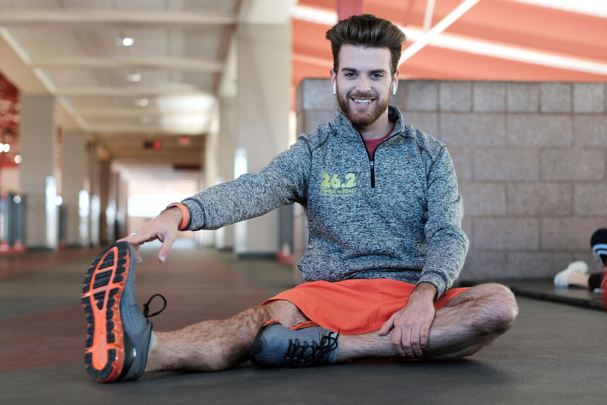 A runner sits on an indoor track stretching his right leg.