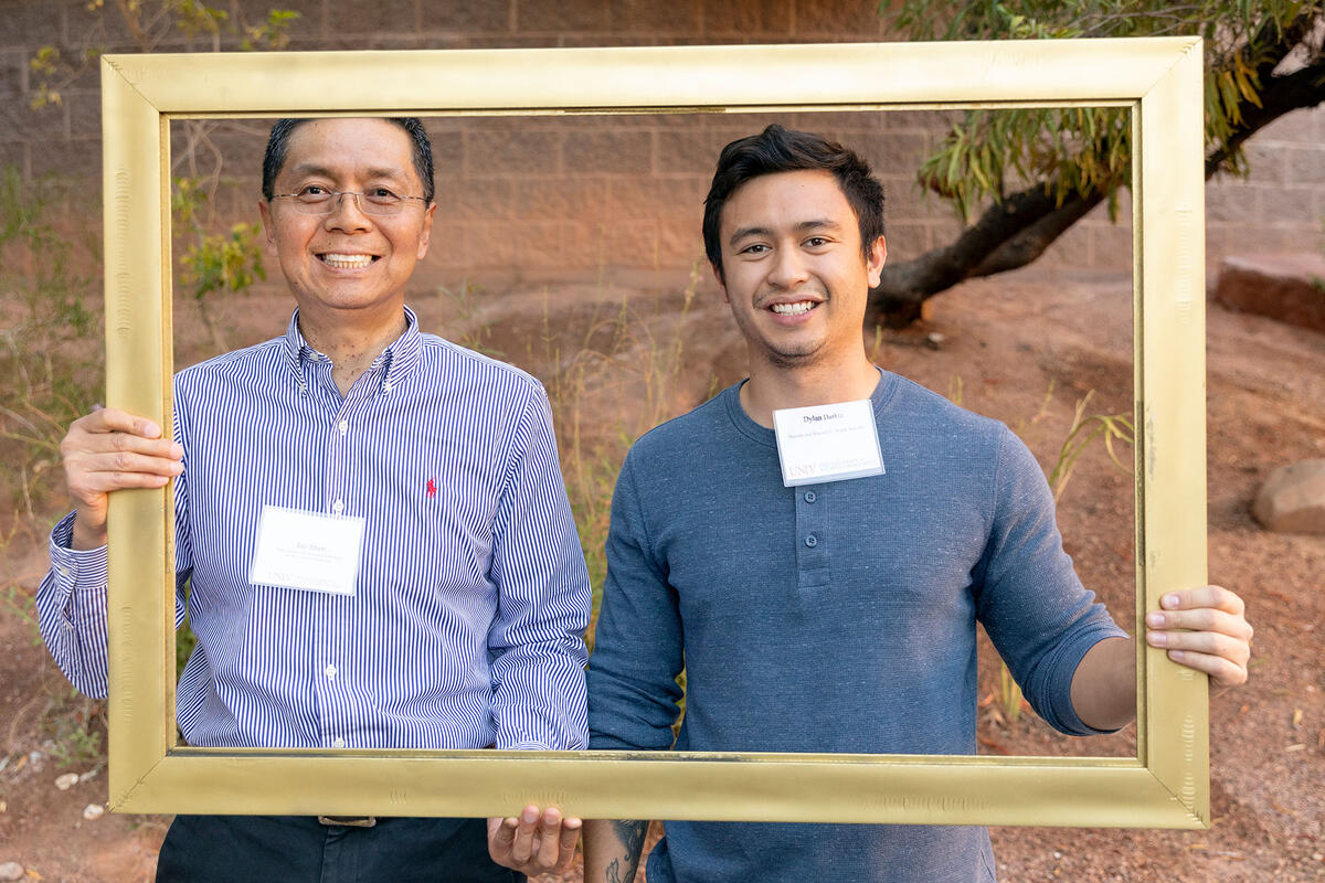 Two males smiling while holding a frame