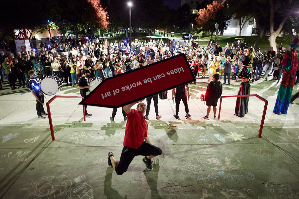 A person performing with a signage in front of a crowd.