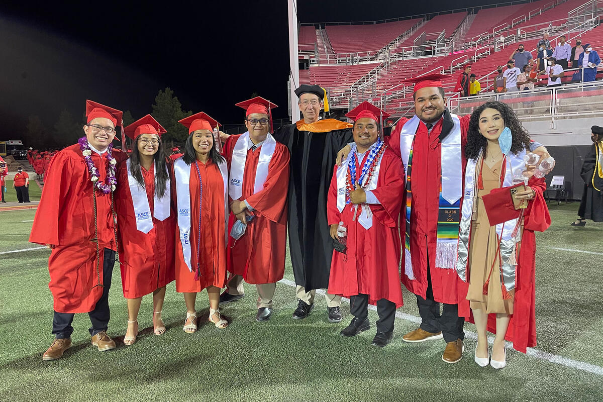 Seven graduates standing with a professor at a commencement ceremony