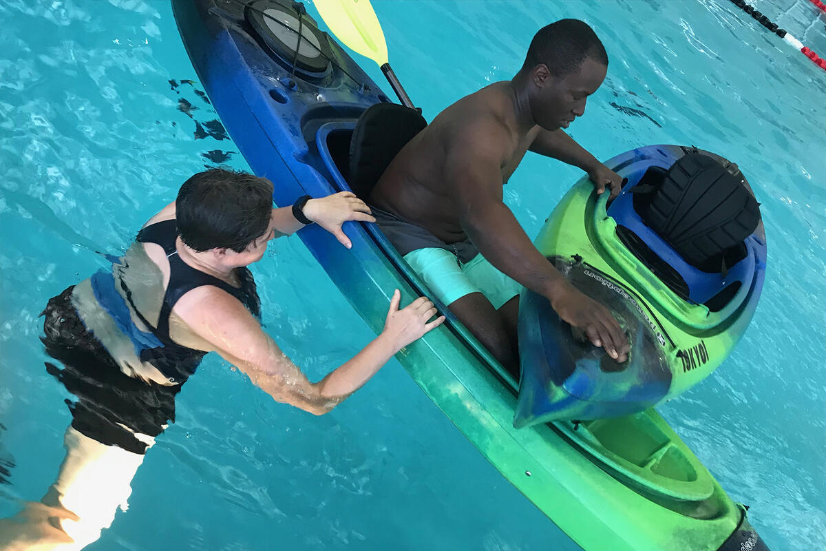 A man on a kayak and another man in the water.
