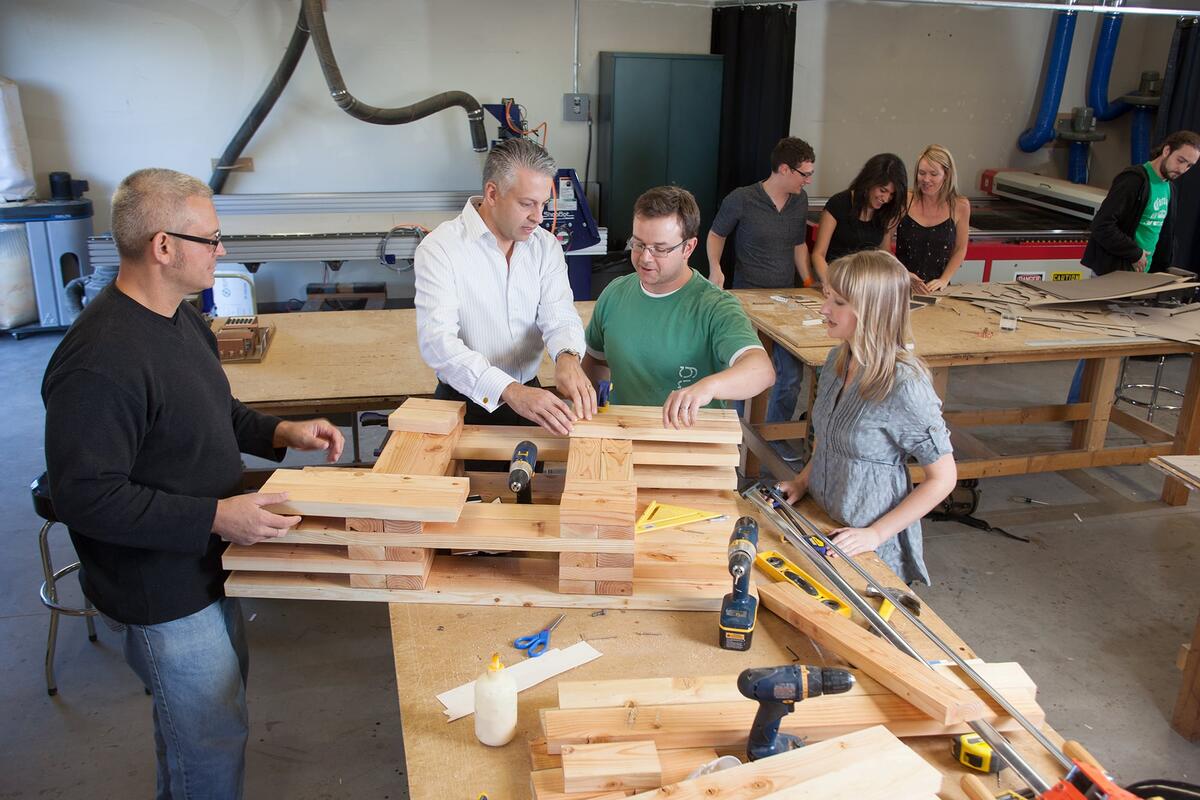 An instructor working with students on a project designing something with wood pieces.