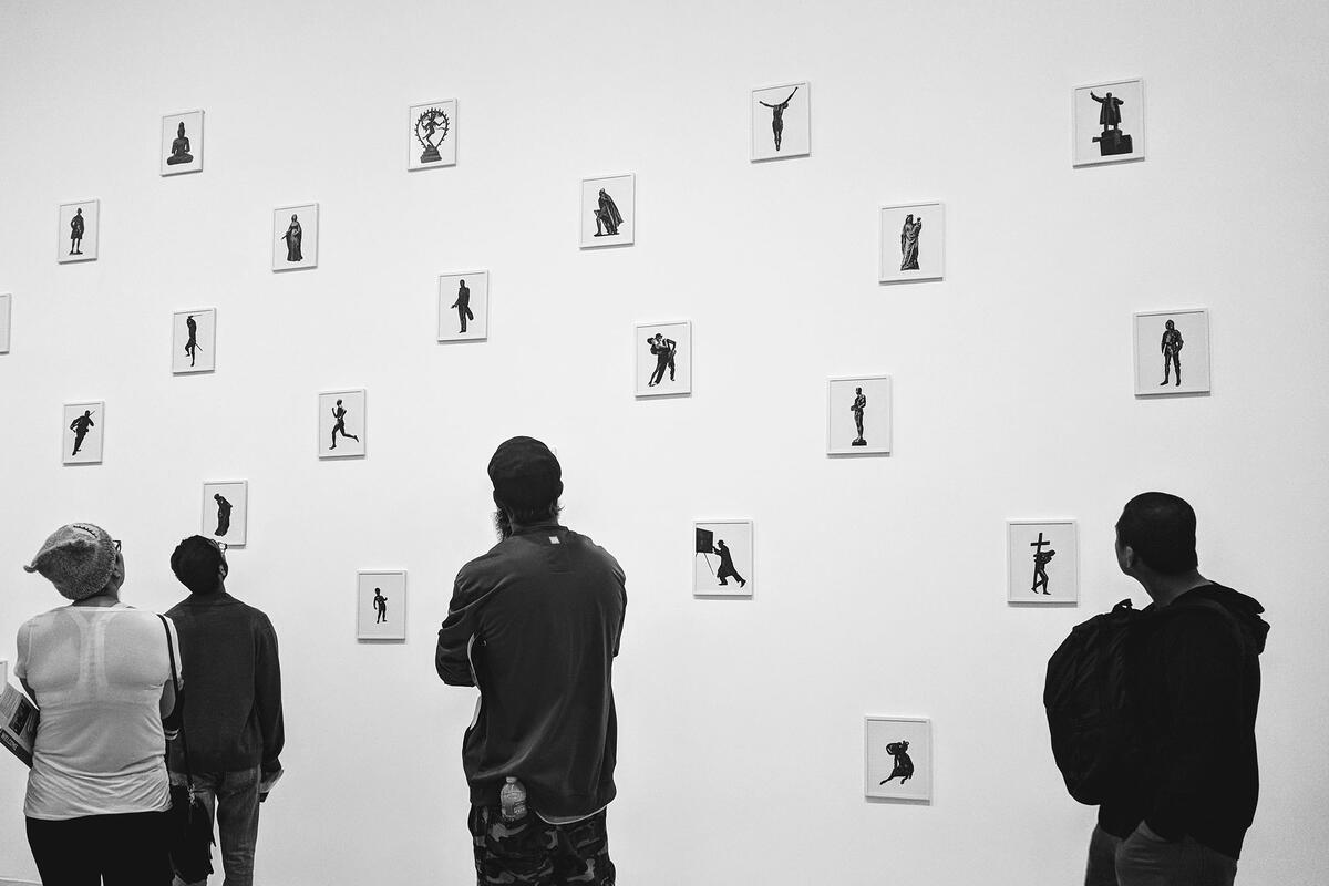 Black and white of a group of four people looking at numerous polaroid-sized images hanging on a wall