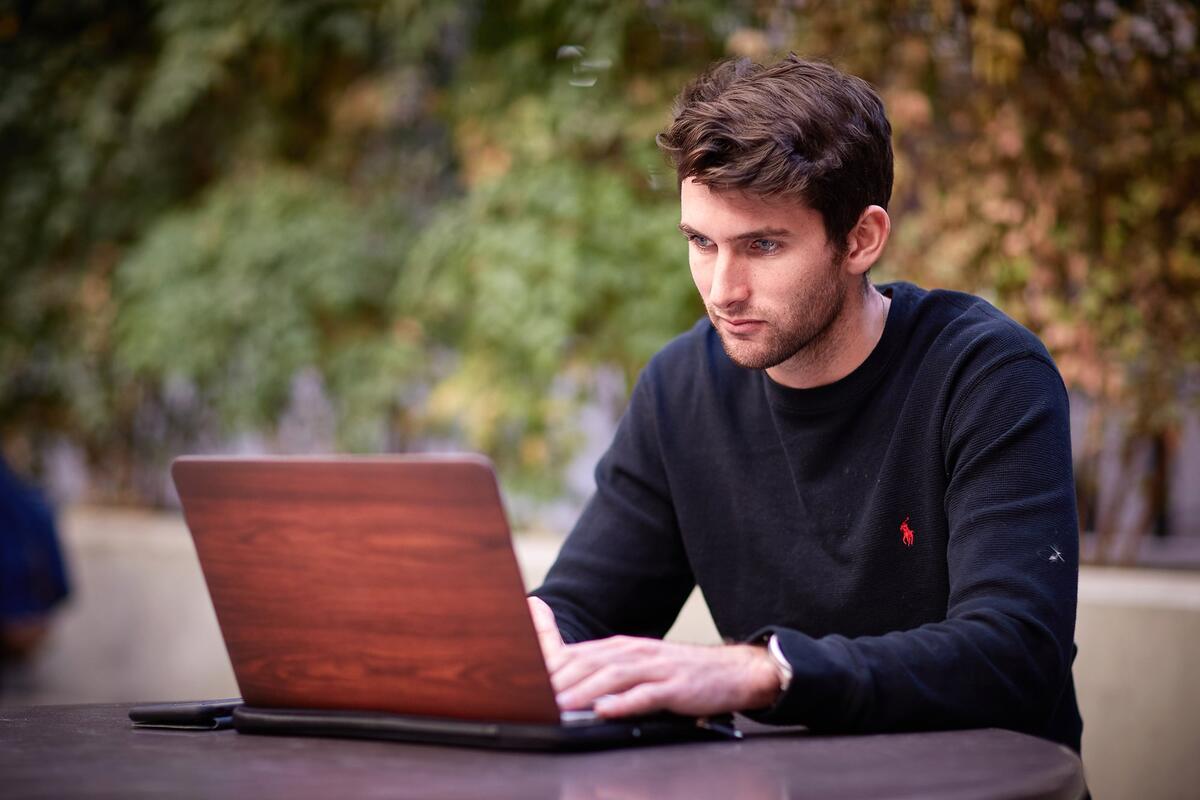A business student working on his laptop outside.