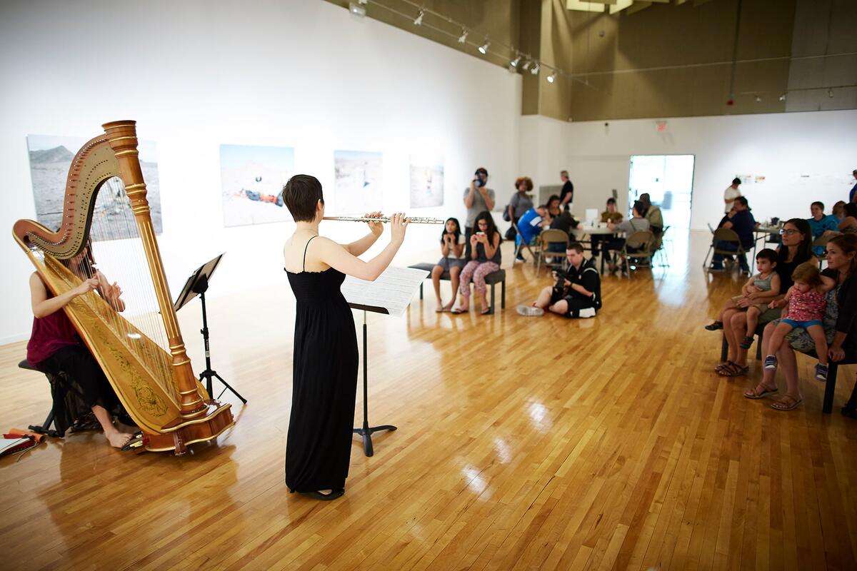 A flutist and harpist playing at a gallery.