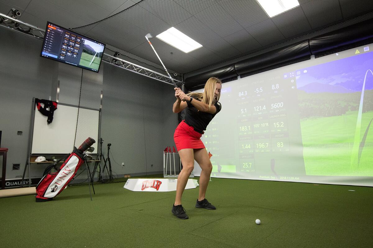 A student swinging in a indoor golf simulator.