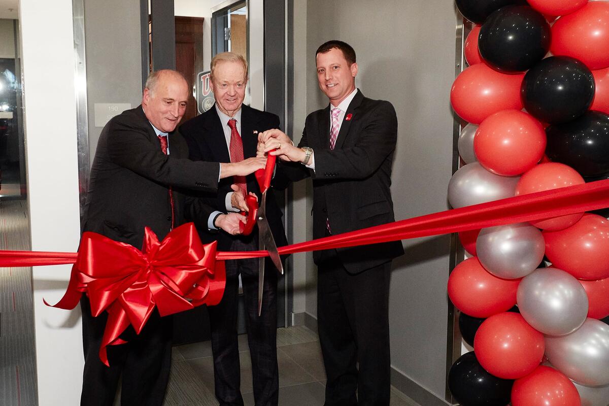 Men in suits in the Dwaine Knight center cutting a large red ribbon in front of the entrance.