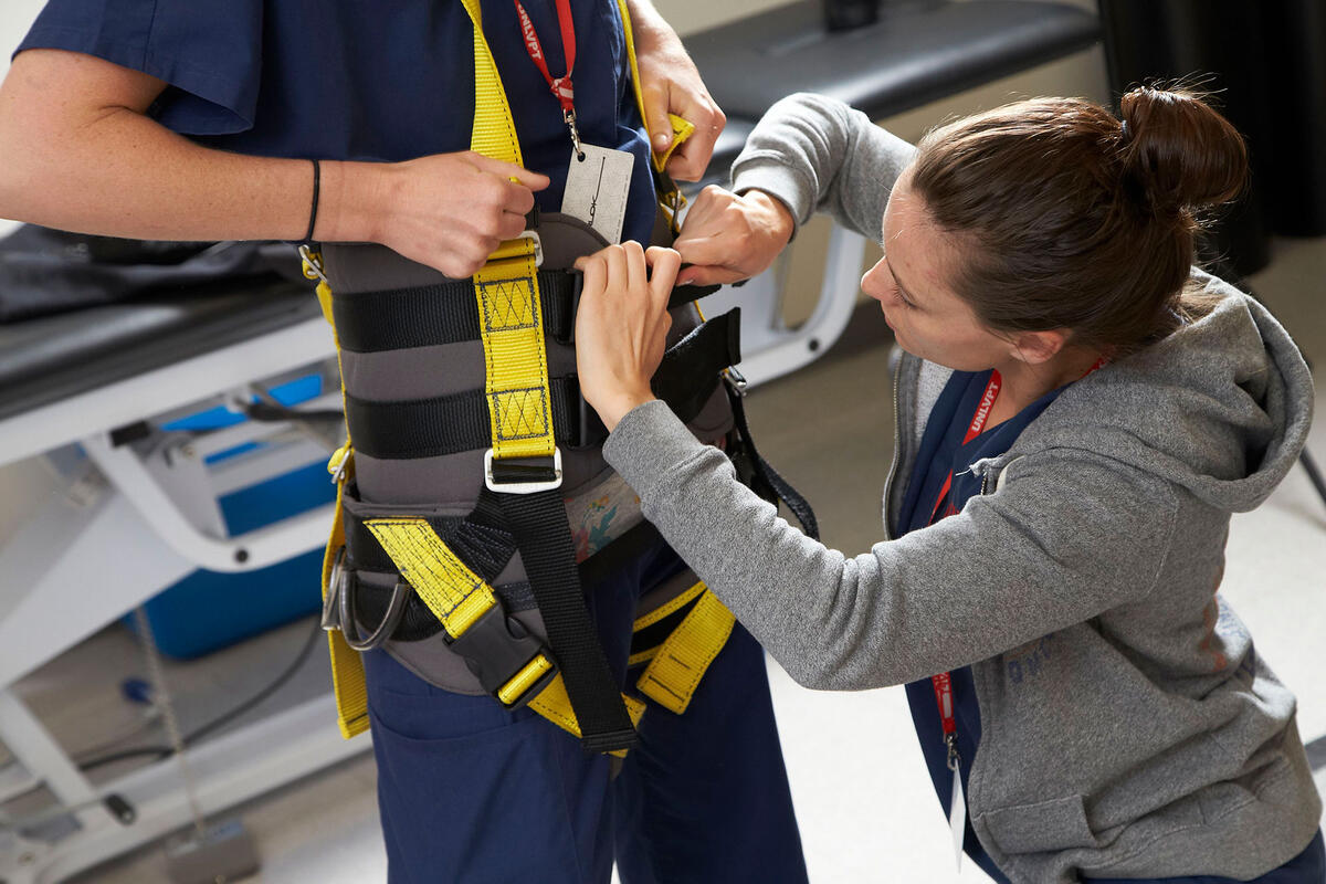 Female physical therapist strapping a person in to a safety harness