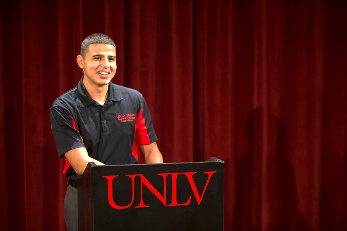 A student doing a mock debate at a podium with UNLV on it.