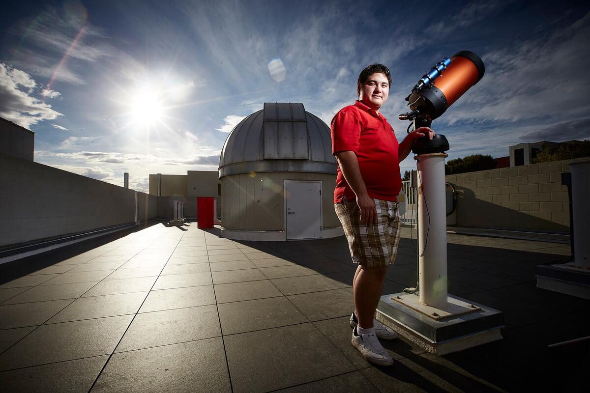 Student standing in from of telescope at sunset