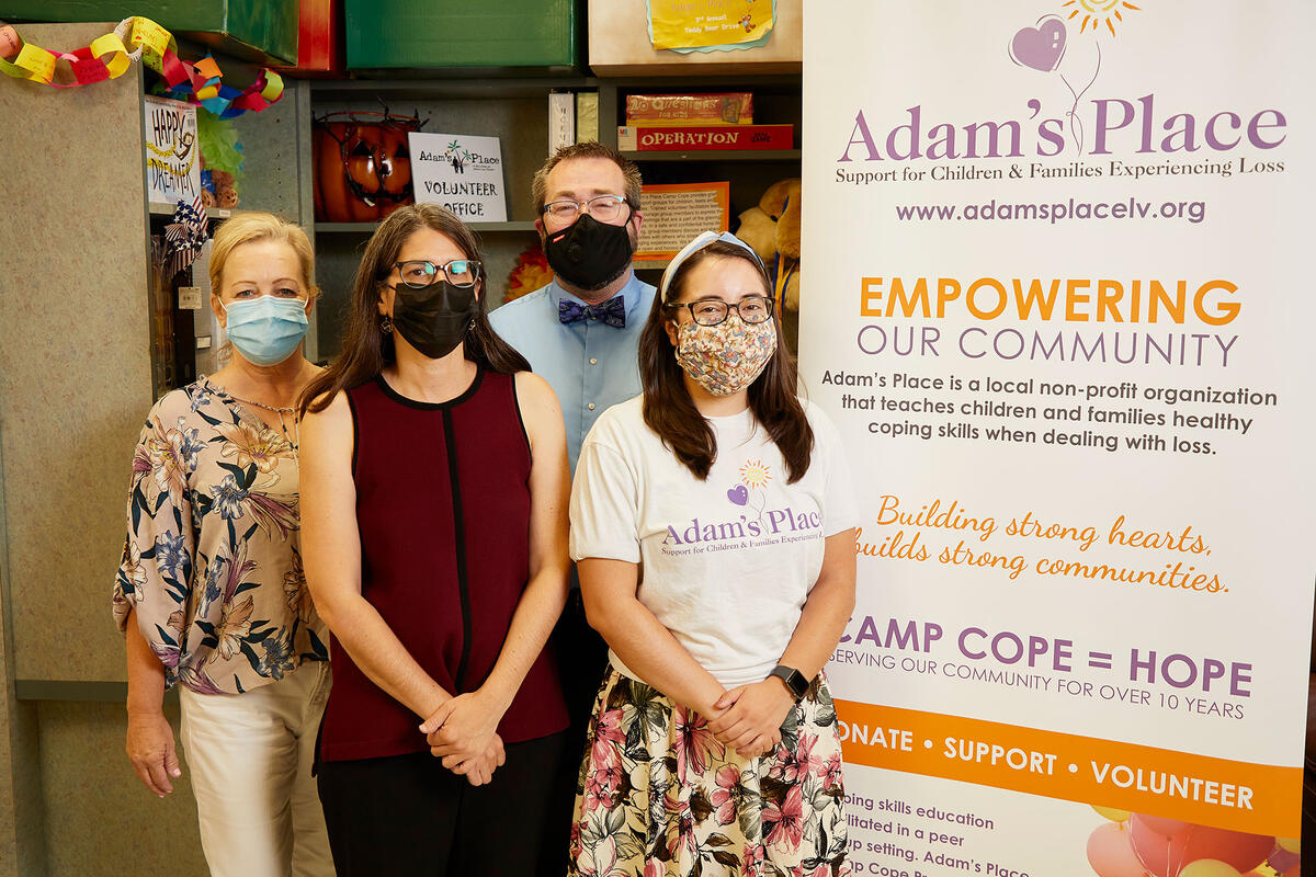 Four people with masks standing besides a sign.
