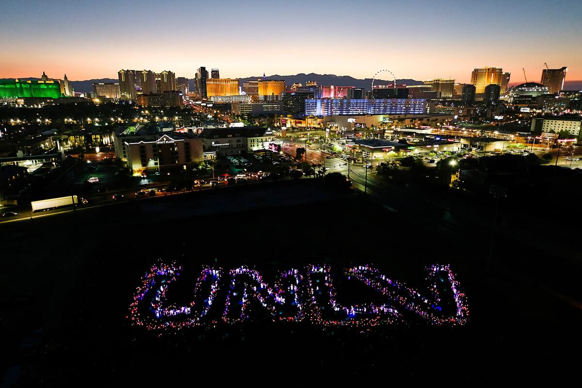 Crowd, holding lights, spell out U-N-L-V with the Las Vegas Strip in the background.