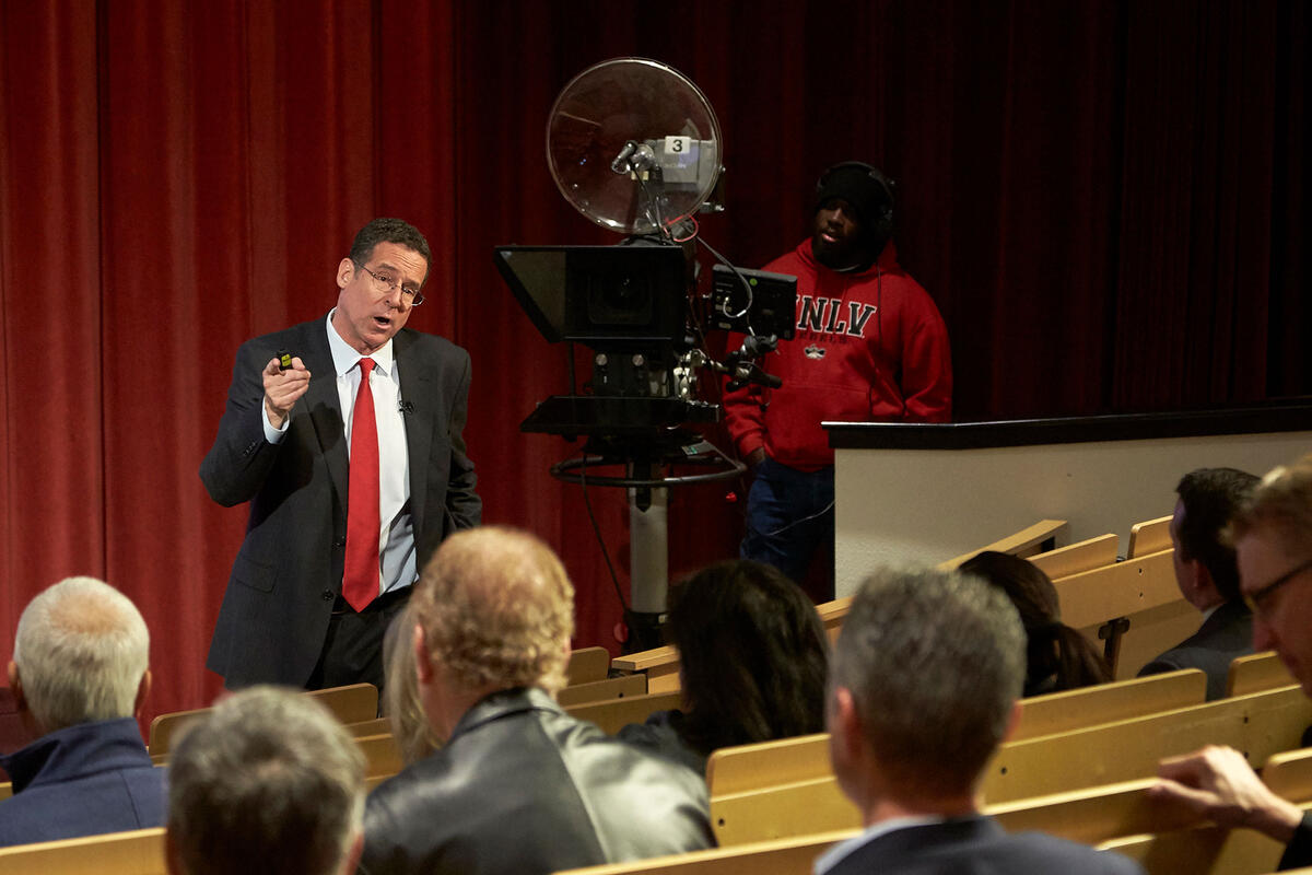 A man speaking in front of audience on stage. 