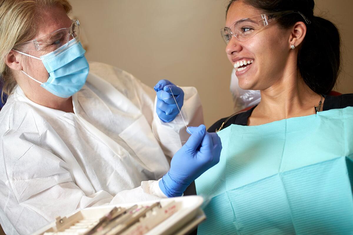 A masked dentist holding floss with smiling patient.