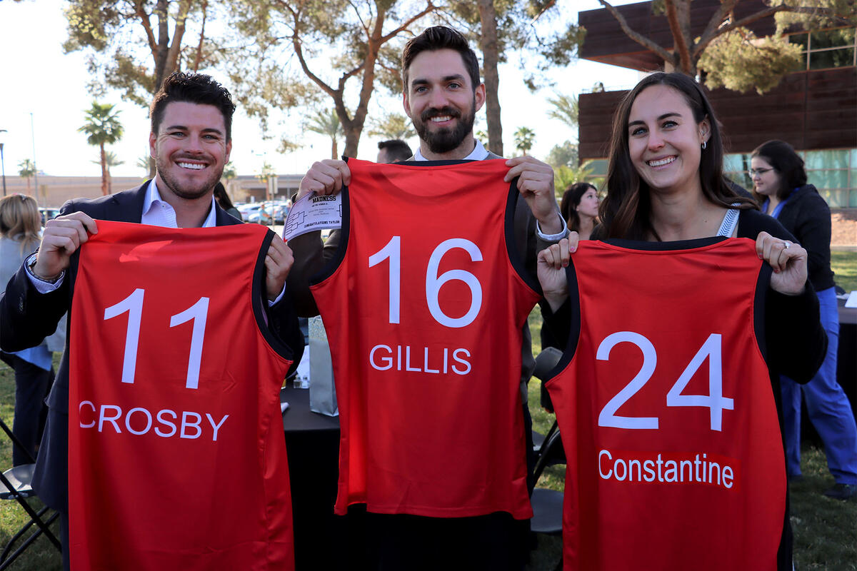 three students holding red jerseys with their names on it