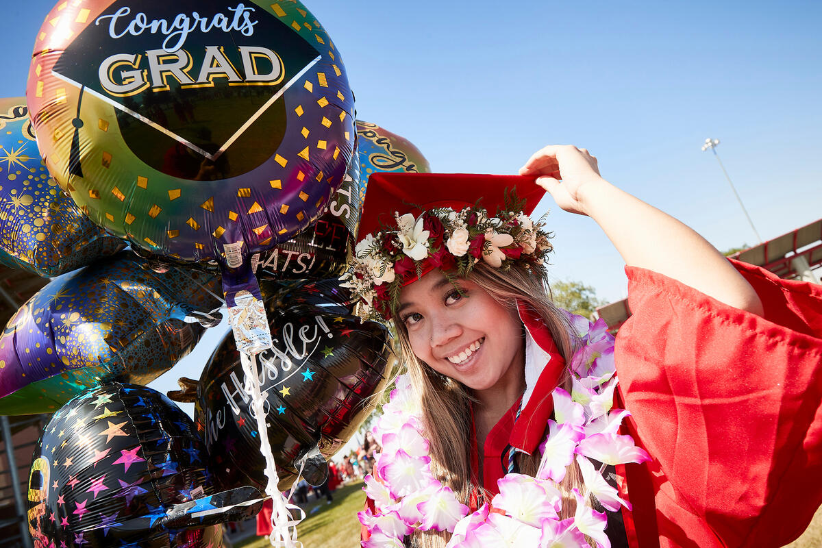 Young woman at commencement holding balloons wearing numerous flower leis