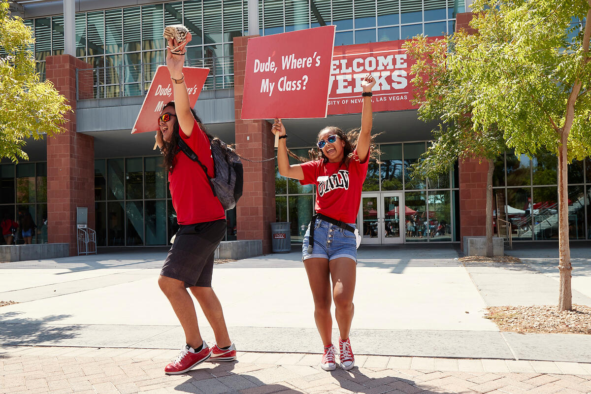 Two students wearing red UNLV shirts and holding up signs that say Dude Where's My Class