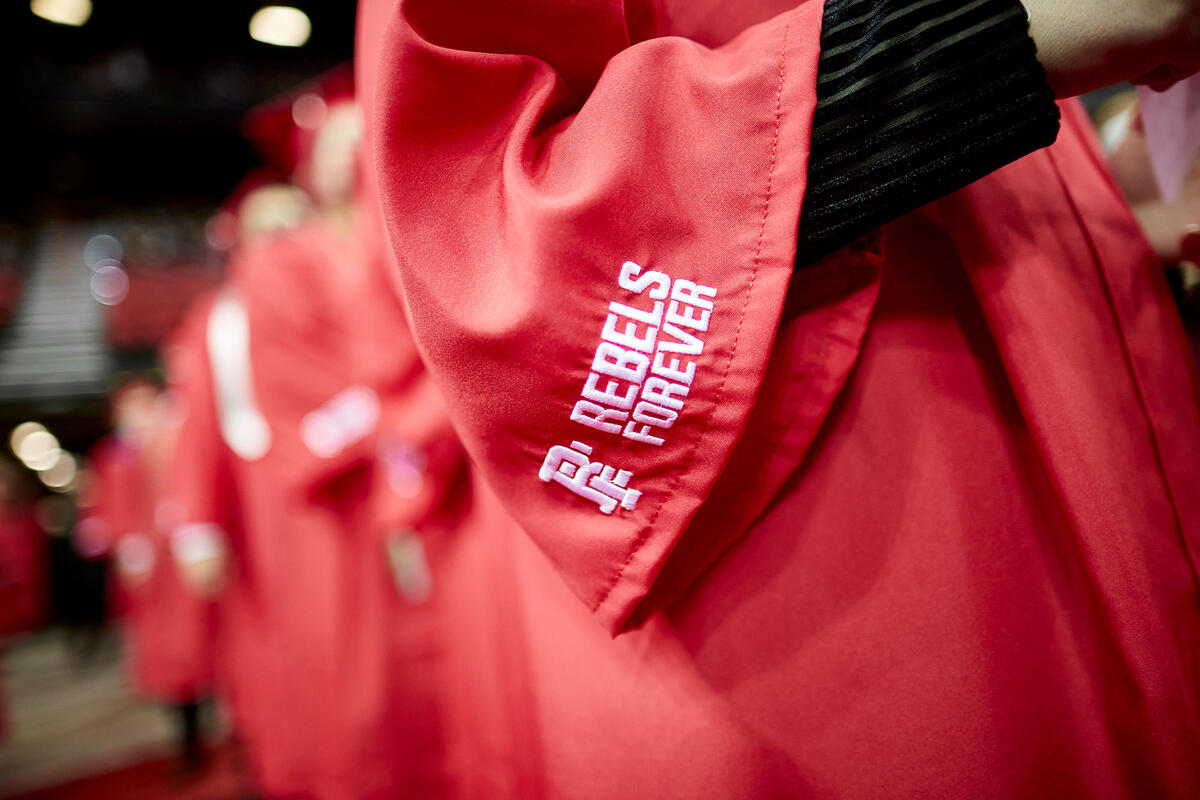 Students in red graduation gowns. A label that says Rebels forever is focused on.