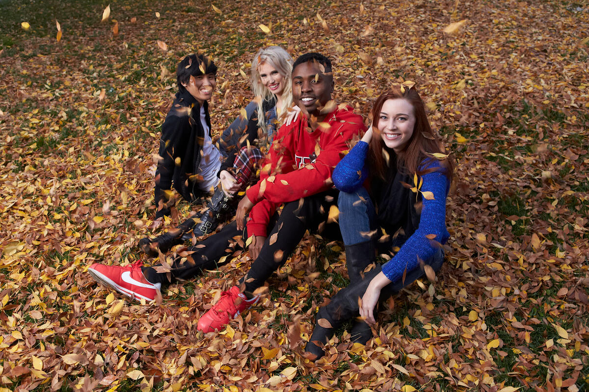 Four people sitting down on the ground covered with a layer of leaves
