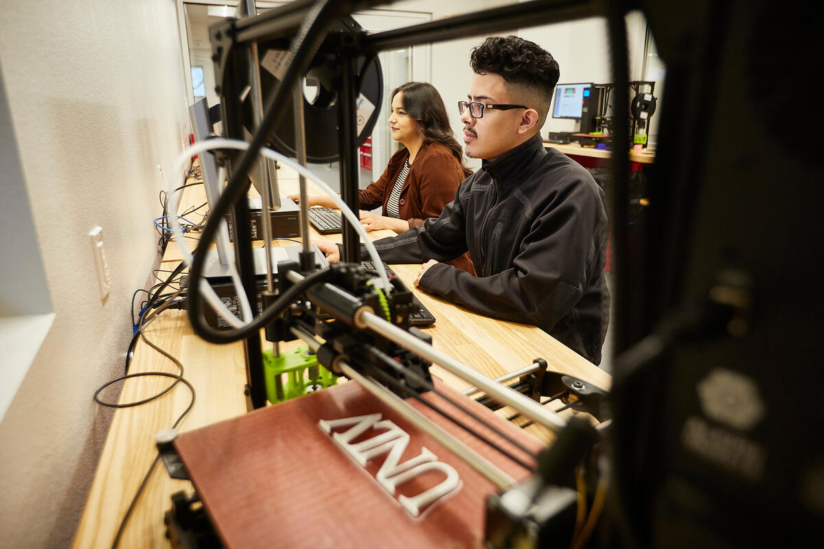 Two students working on a 3D printing machine