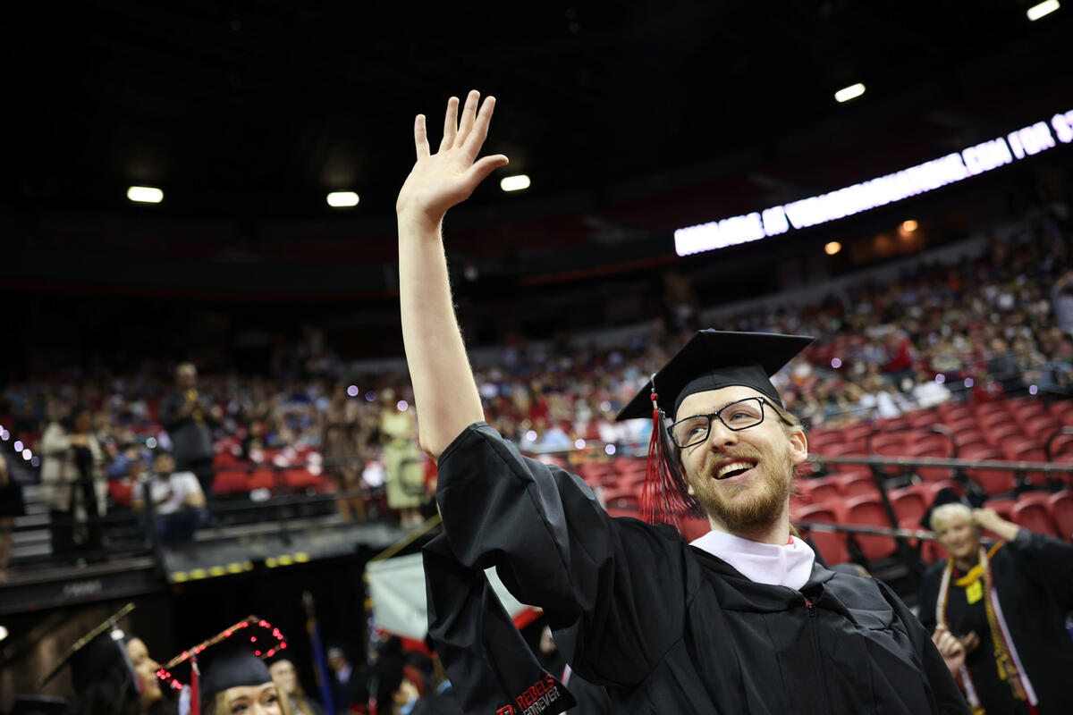 Graduate student at commencement waving to the crowd