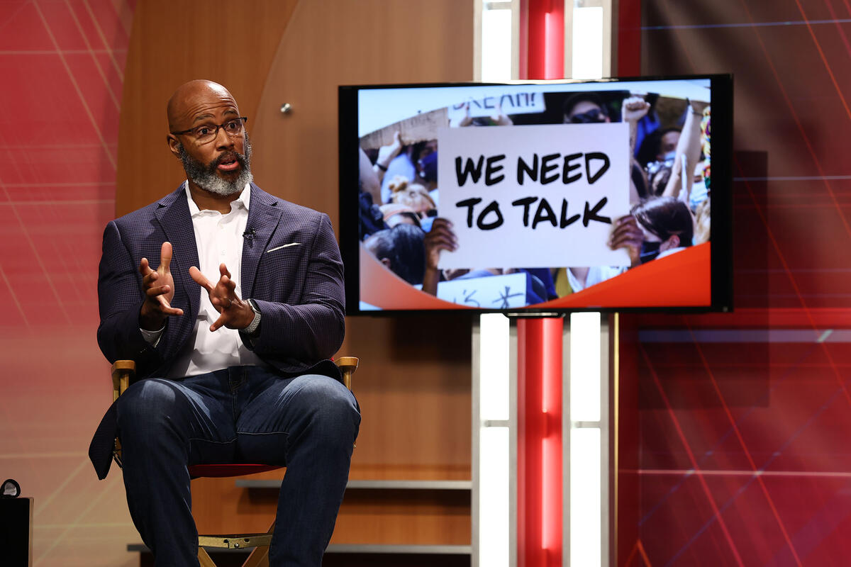 Man sitting and giving a lecture with a screen behind him that says We need to talk.