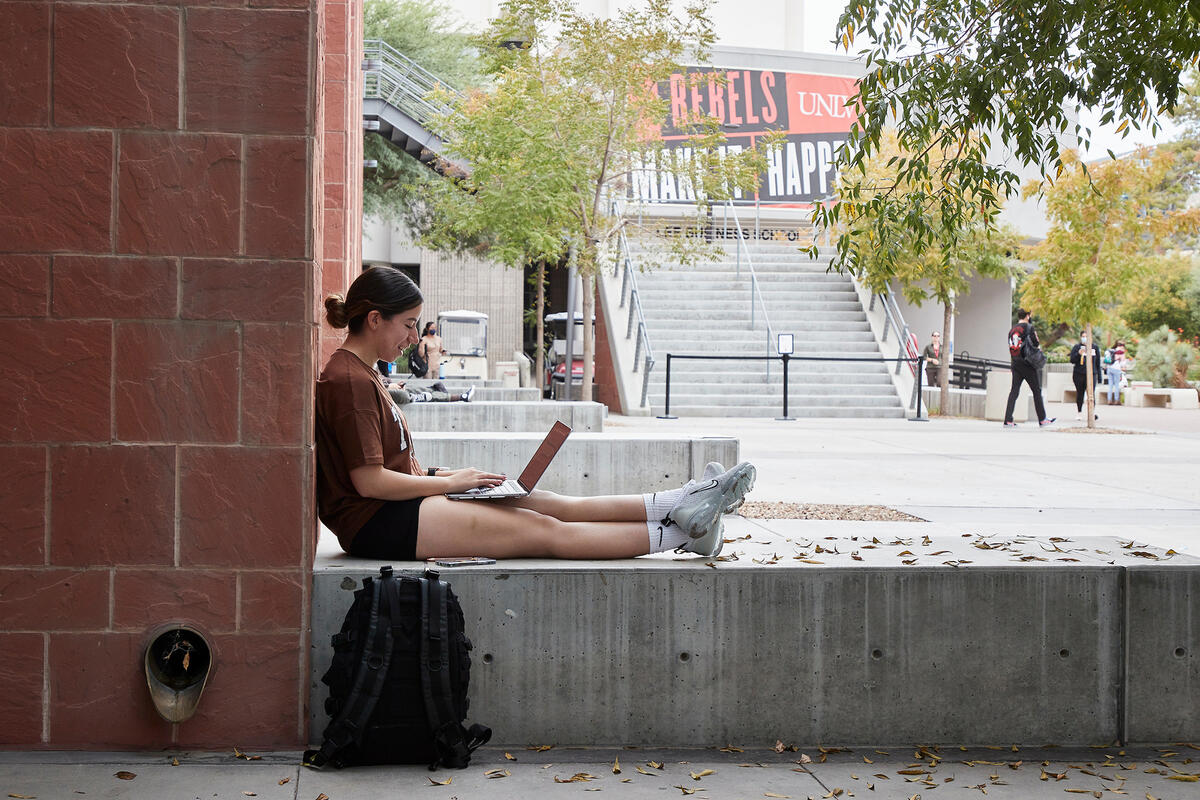 Student sitting on a concrete bench and smiling while working on a laptop