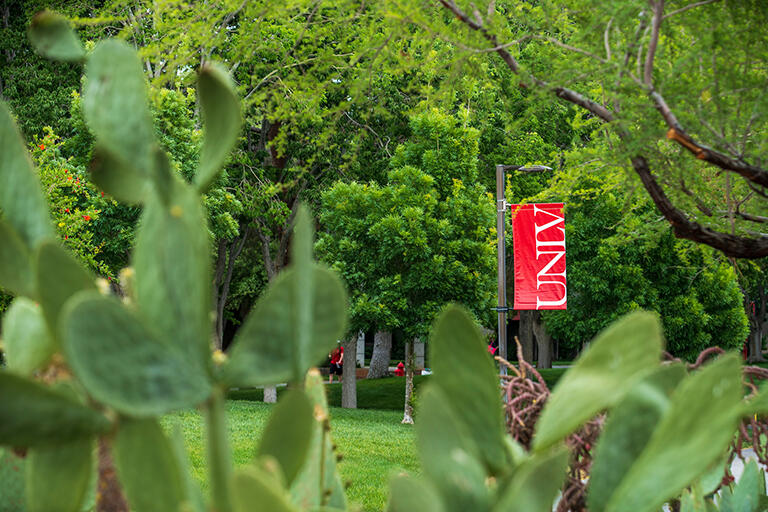 Red U.N.L.V. banner framed by green cacti in the foreground and green trees in the background