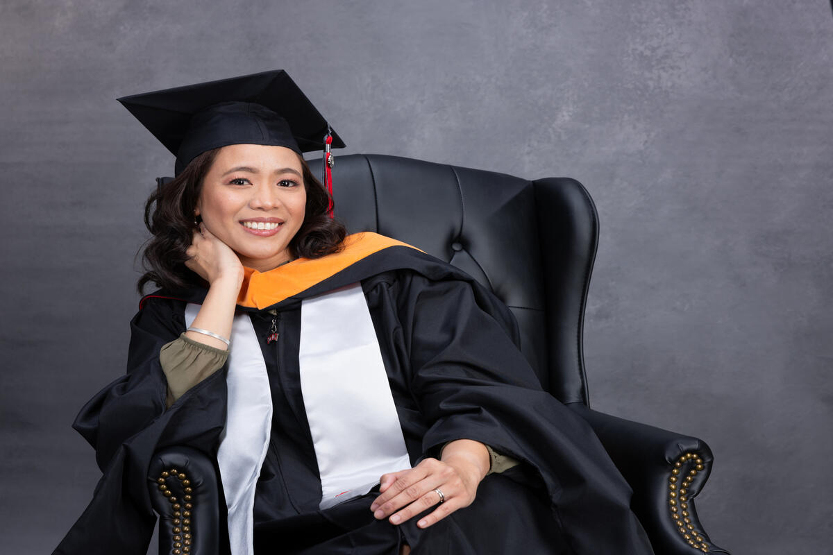 woman dressed in graduation gown and sitting in chair