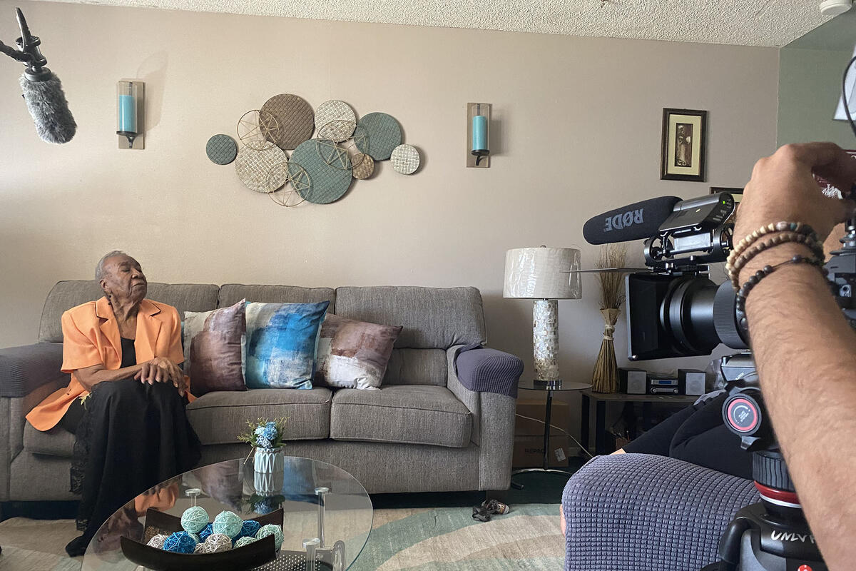older woman being interviewed by film crew in her living room