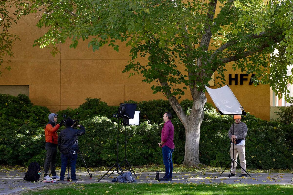 A film crew records an interview on a campus sidewalk.
