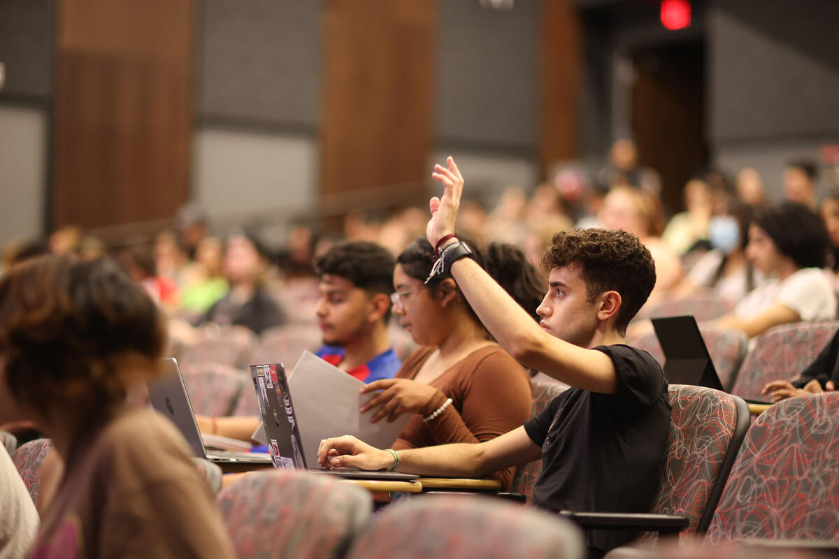 Full lecture hall with student in focus raising hand