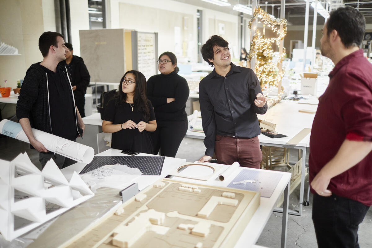 Students at the architectural studio gathered around a table with building models and blueprints.