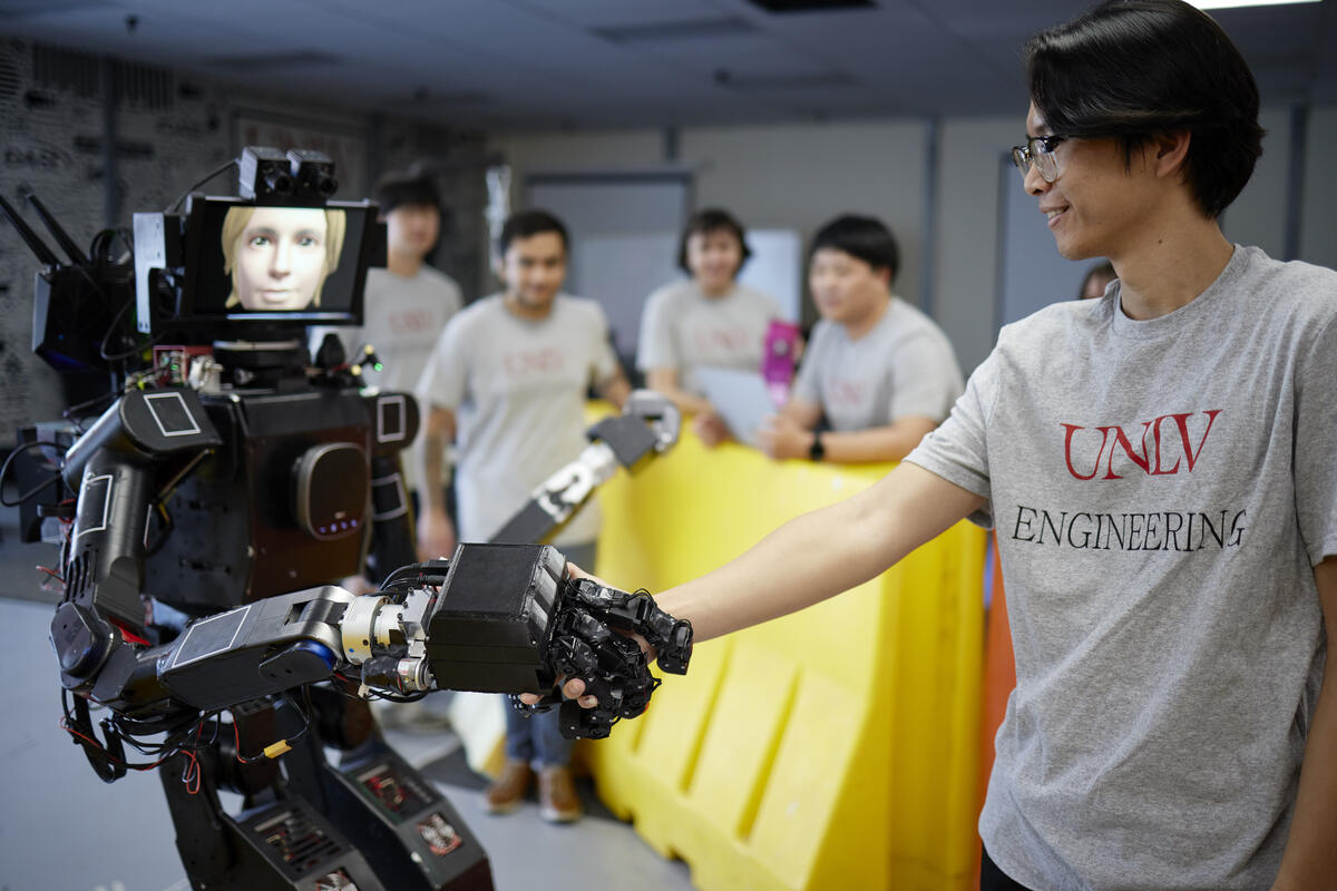 Engineering student shakes hand with a humanoid robot with telepresence.