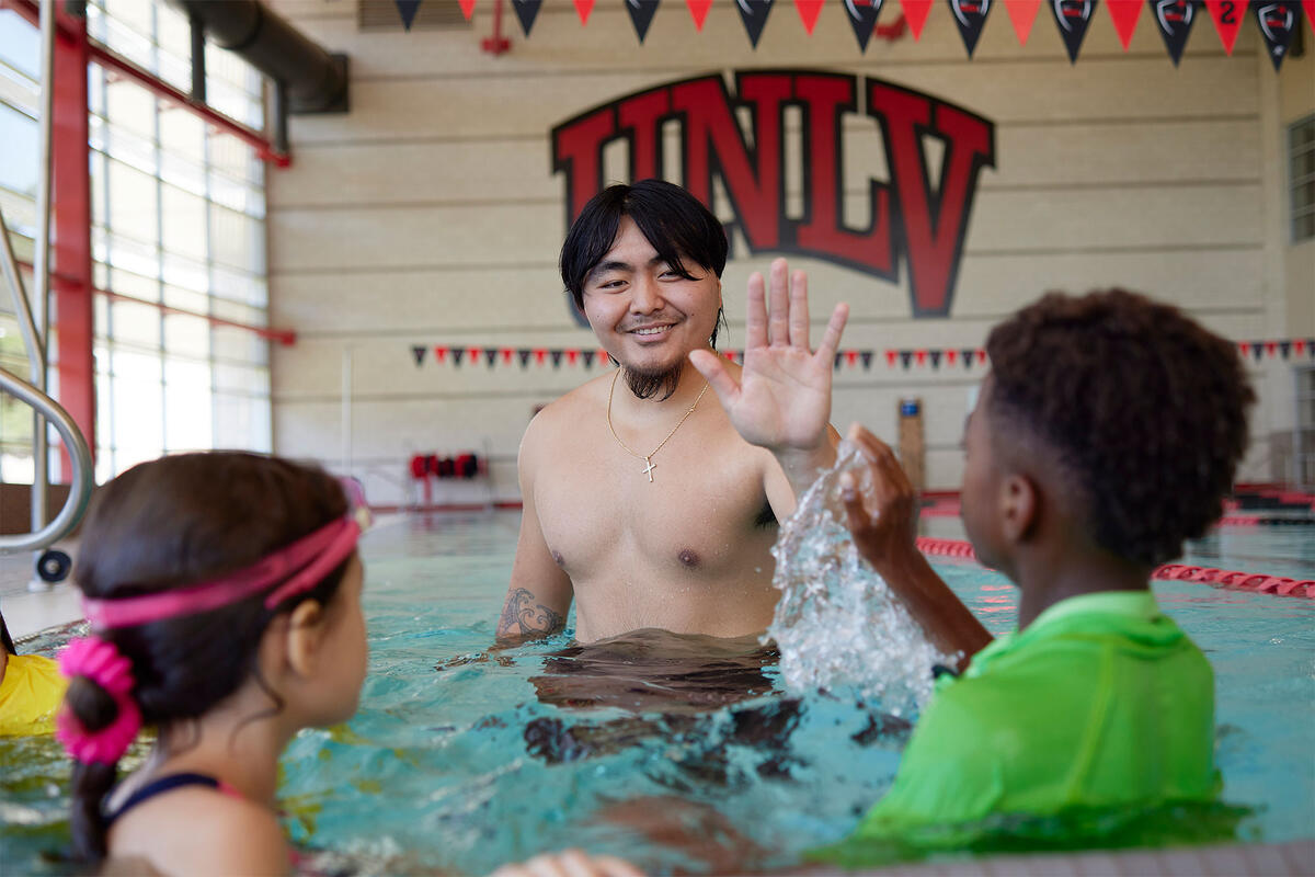 A man and two children in a large pool waving to each other