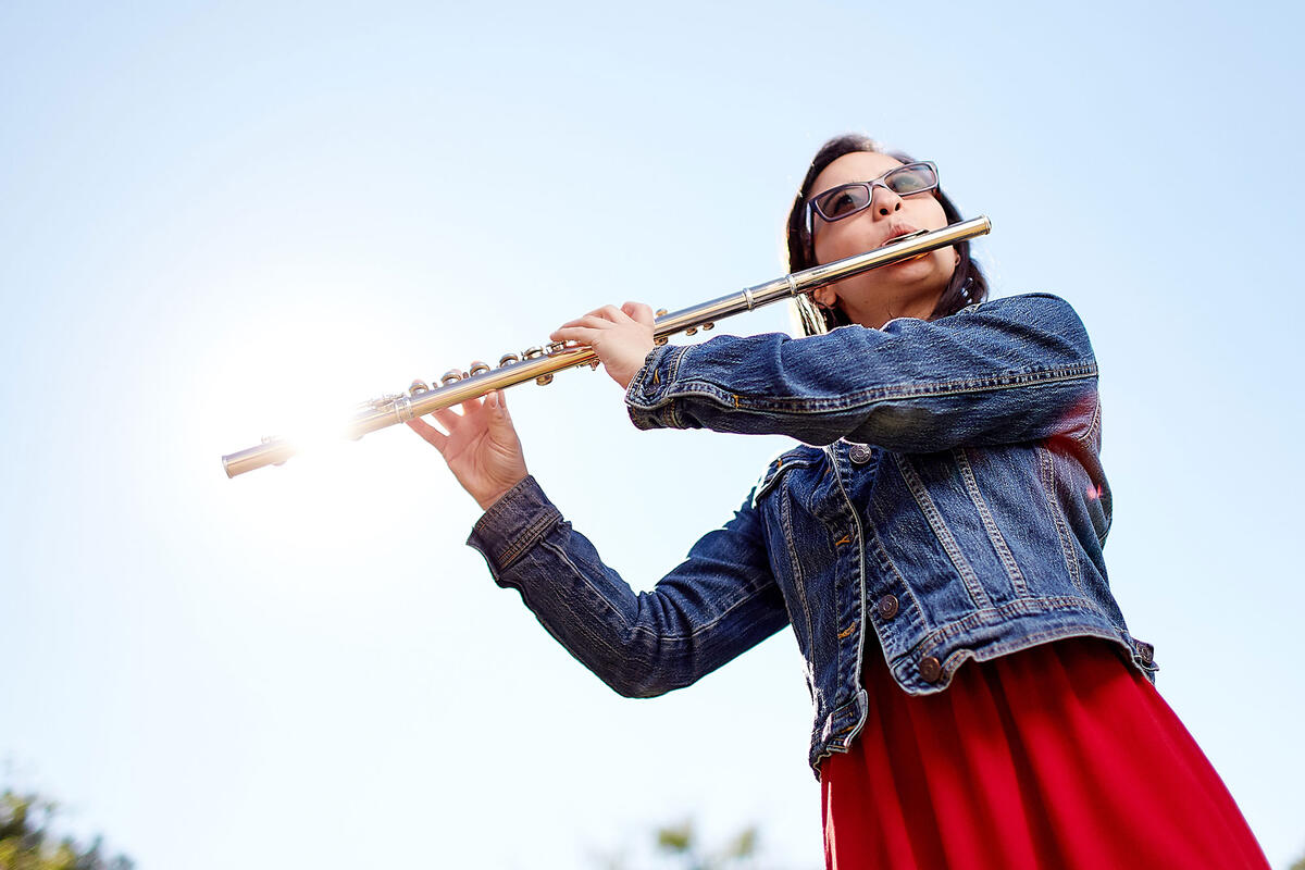 An upward view of a woman playing a flute with the sun gleaming on the end of the flute
