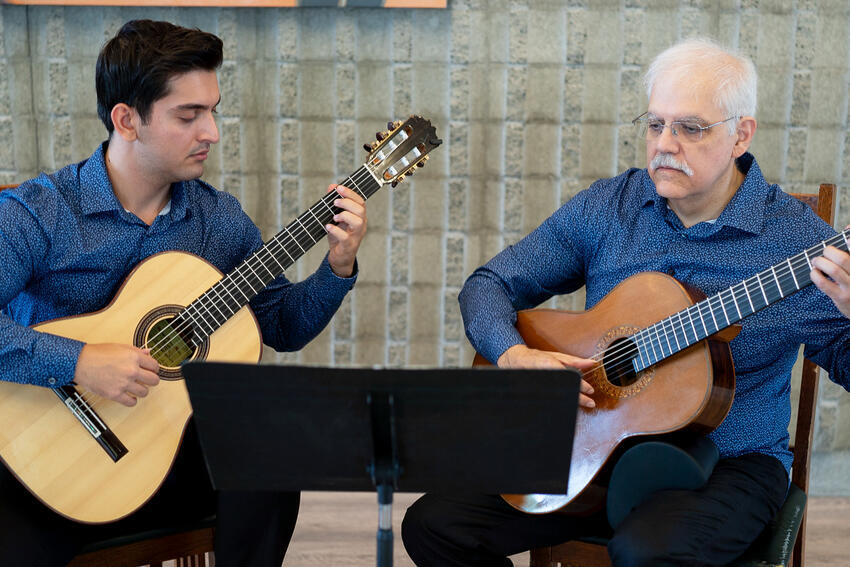 two men sitting and playing acoustic guitars