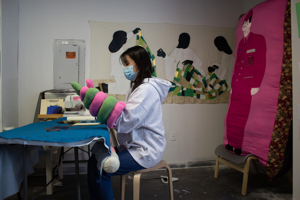 Student working on a quilt like art piece on a table 