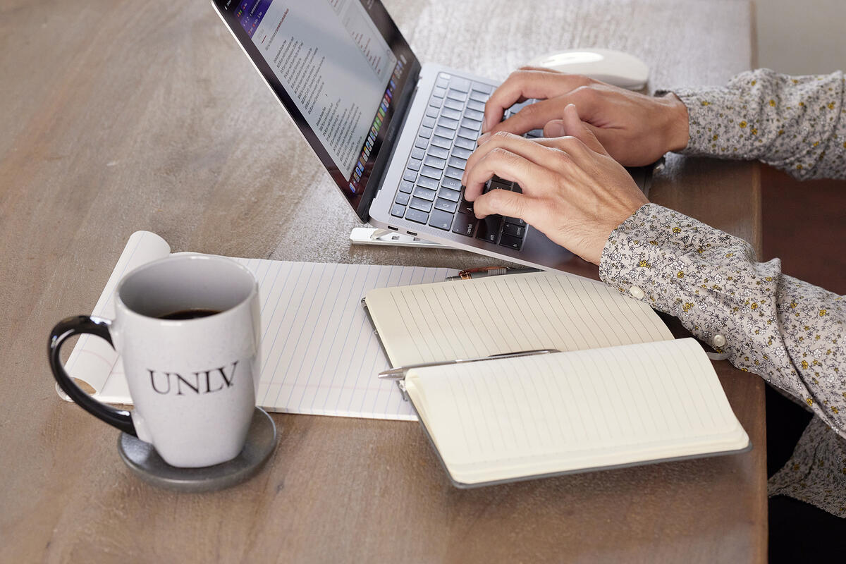 view of a laptop, open notebooks, and a cup with UNLV logo