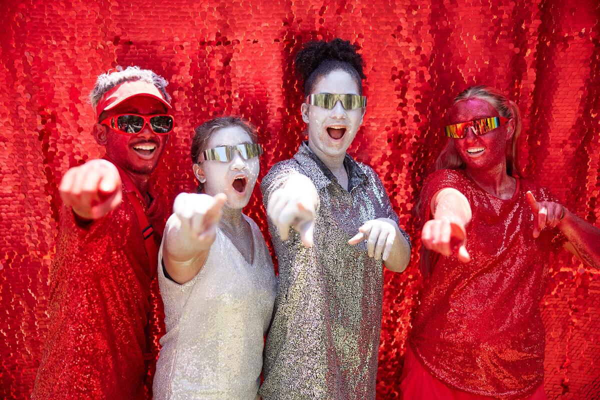 Four students, covered in red and silver clothes and glitter makeup pose for the camera