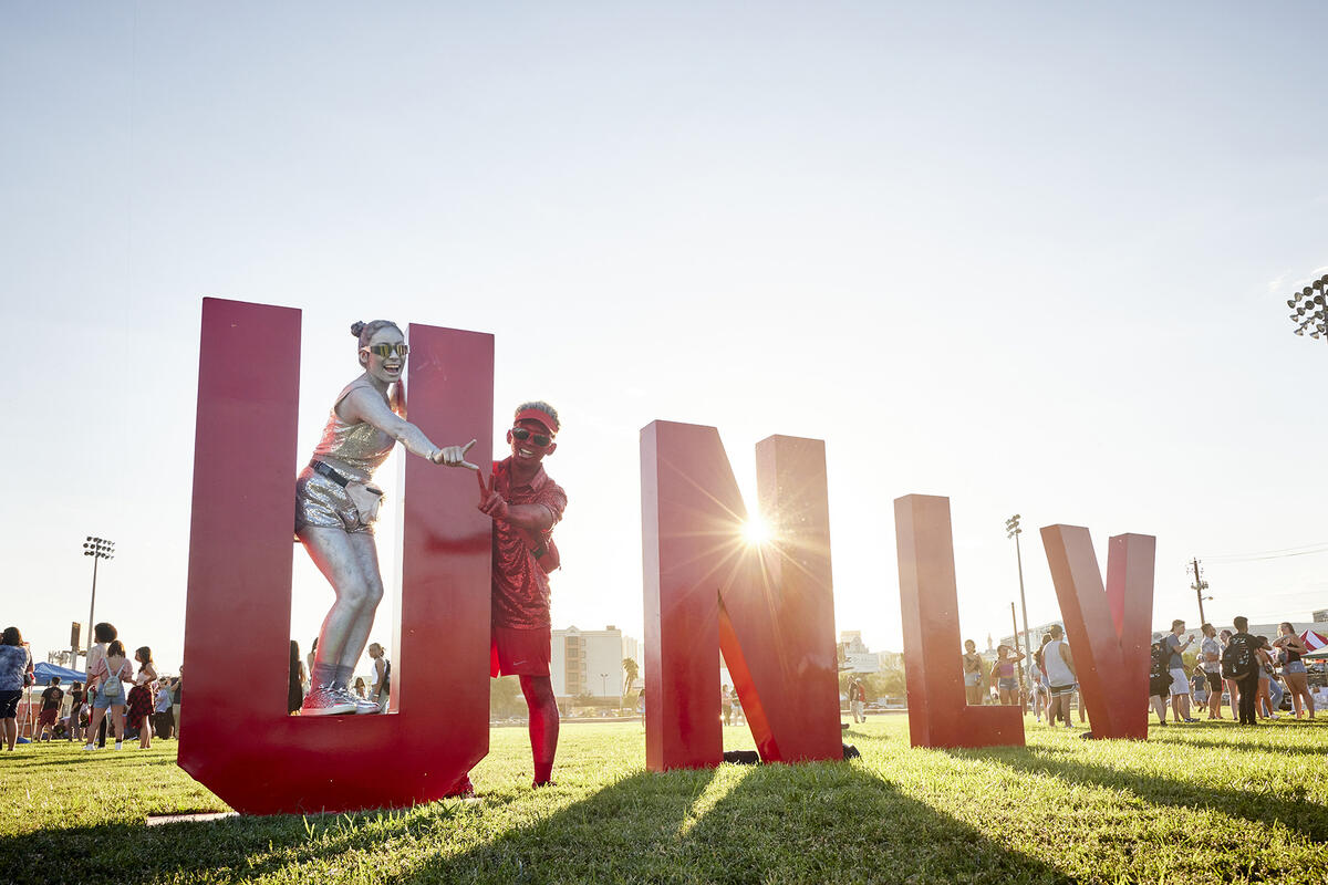two people holding up hand signs and posing with large letter displayed UNLV