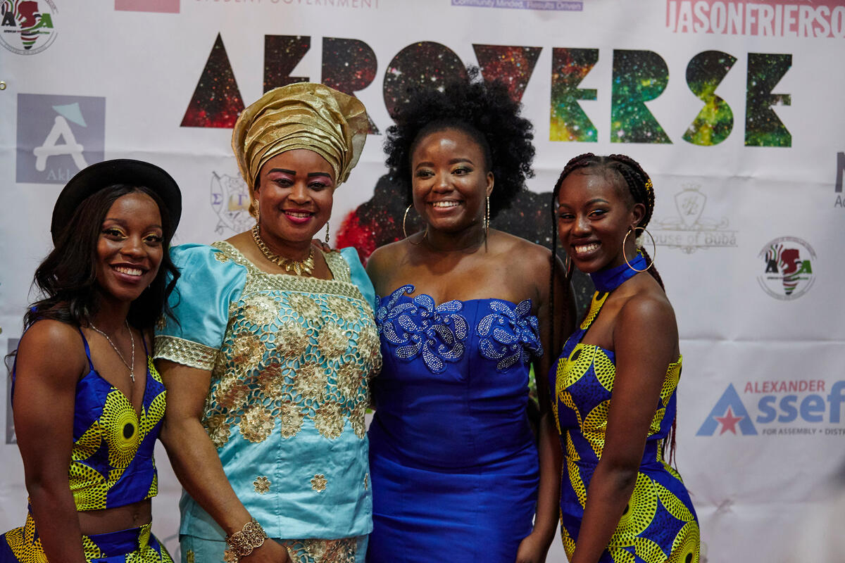 Group of four women of African descent wearing elaborate dresses of various blues and golds