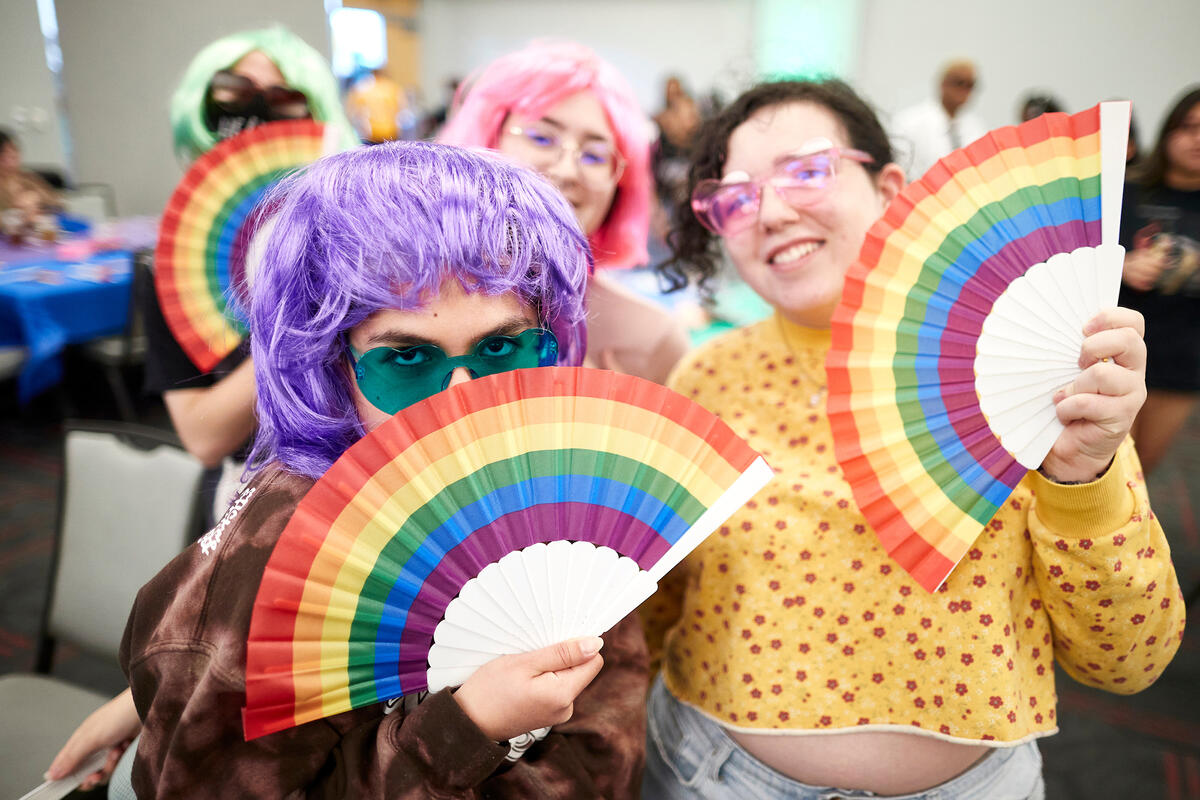 Students from the LGBTQ community posing with colorful wigs, glasses, and fans