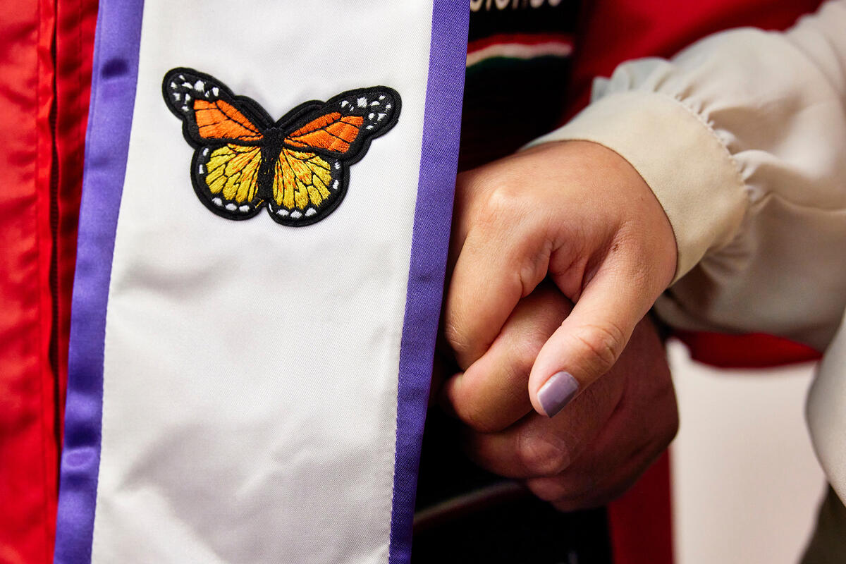 Close-up of the commencement butterfly sash for dreamers of the undocumented student program, the graduate is holding hands with another