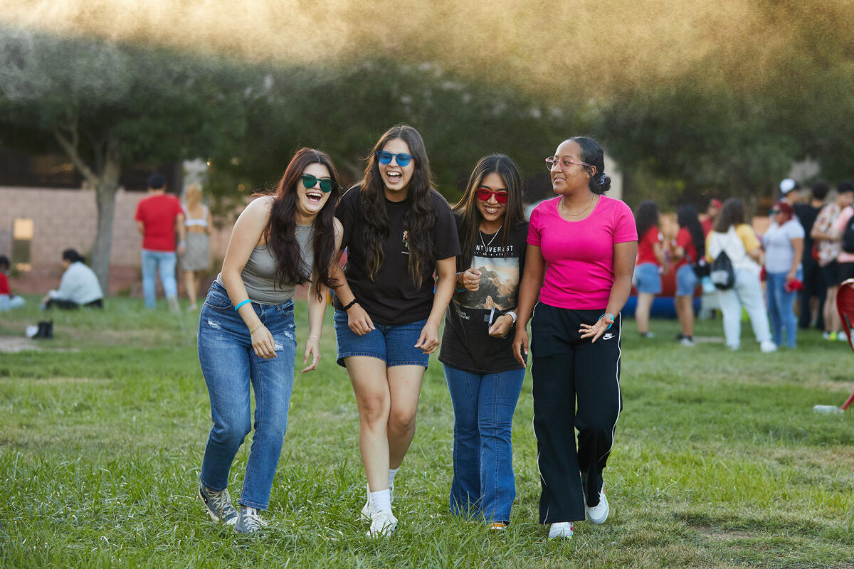 four people walking and laughing on green grass