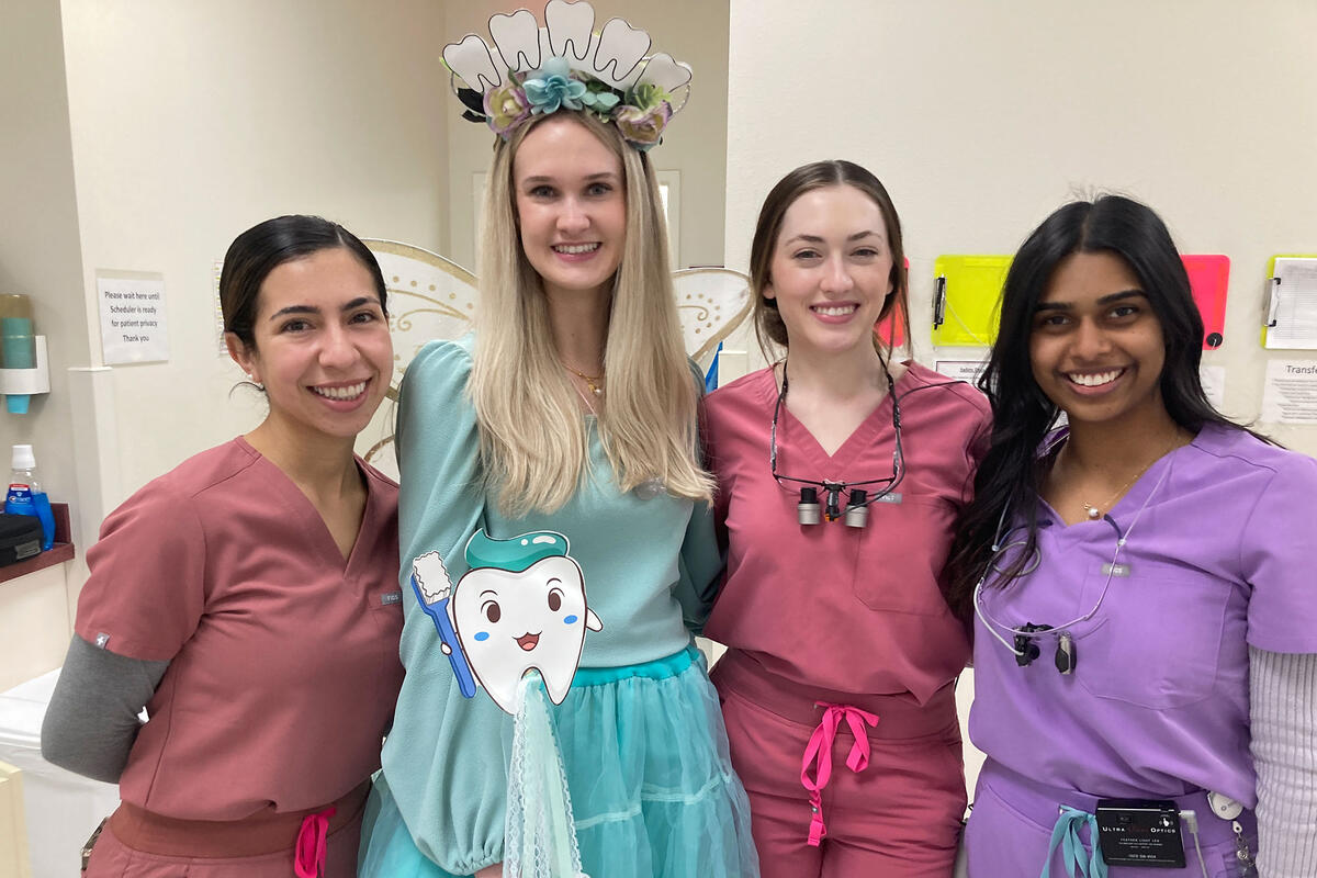 Four individuals smiling (three in scrubs and one dressed up as a fairy)