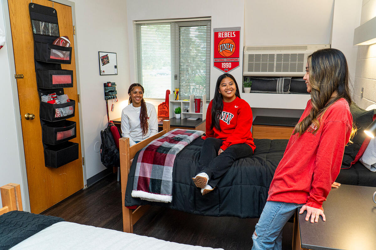 Three students hanging around in a dorm room.