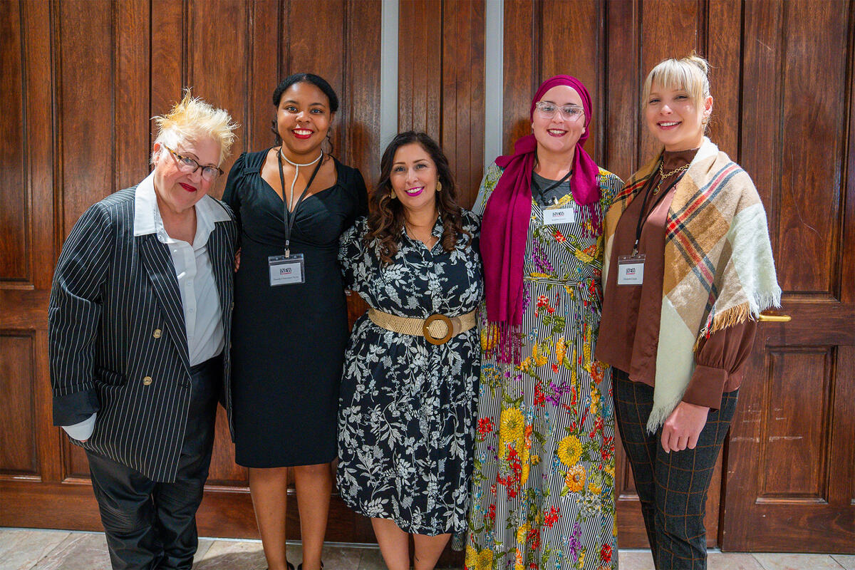 Five women standing in front of a wooden wall smiling