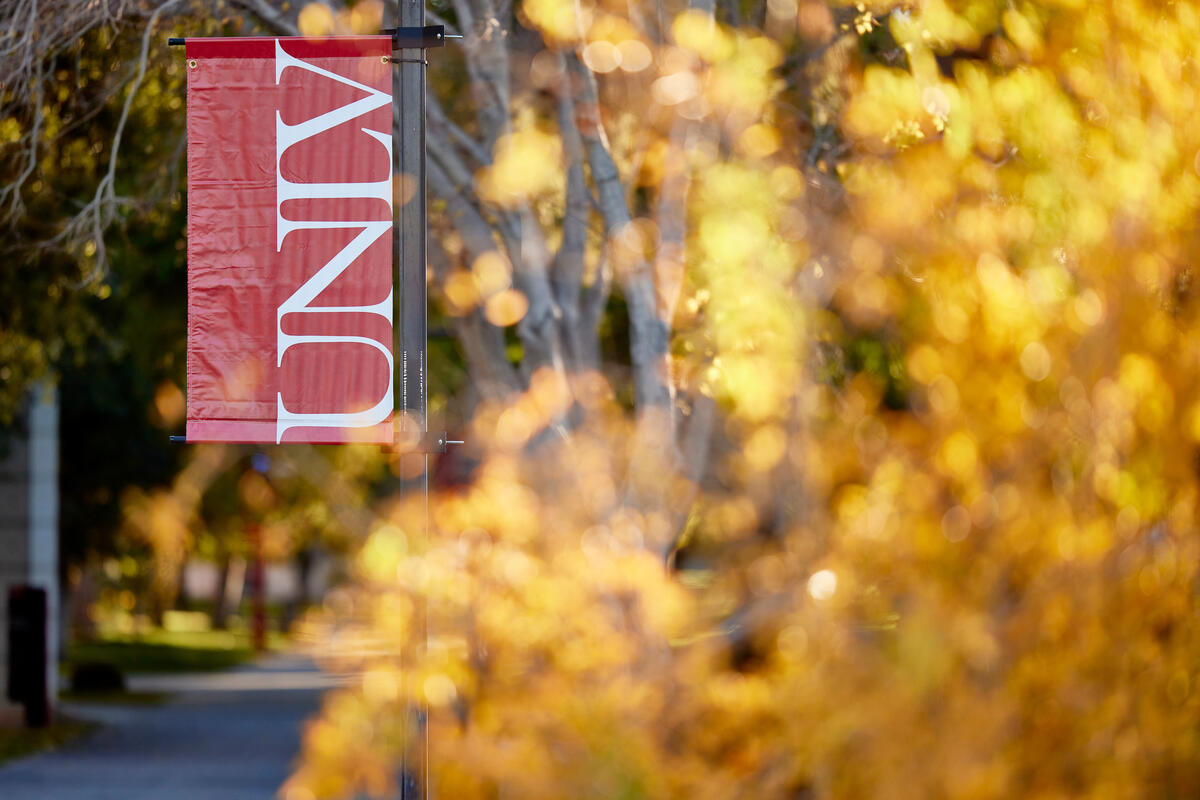 Red UNLV banner amidst fall foliage