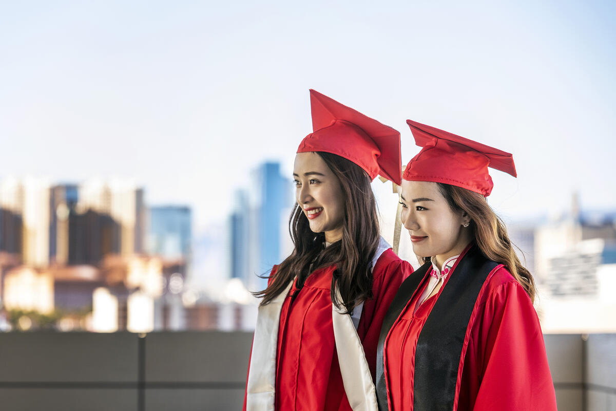 Two women walking wearing UNLV graduation gowns